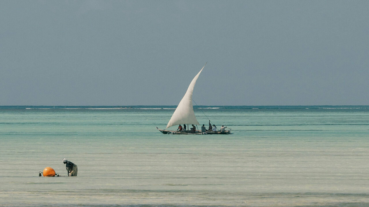 A traditional sailing dhow glides across calm, grey-green water off Zanzibar, Tanzania, on a luxury safari holiday.