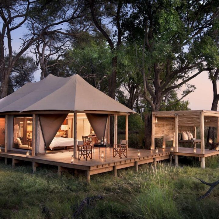 A tented suite stands raised on decking at blue hour at this luxury safari camp, andBeyond Nxabega, Botswana.