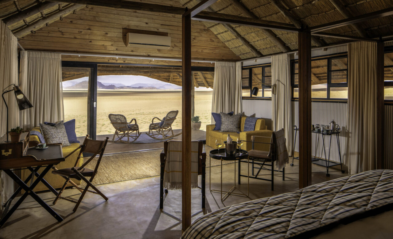 An open-sided thatched suite with a large bed and lounge area looks out over the desert at Kwessi Dunes, Namibia.