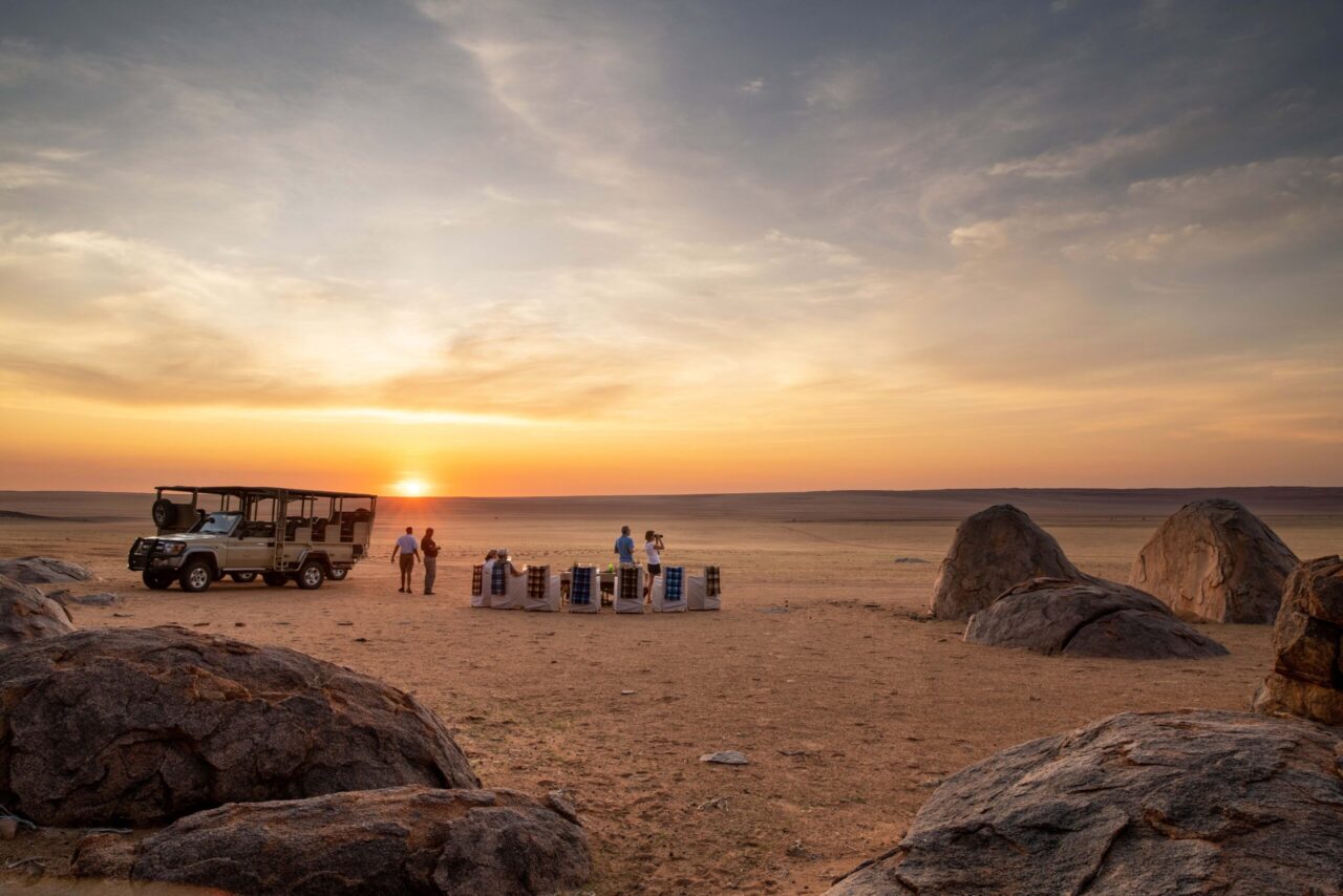 A group enjoys sundowner drinks among red desert dunes at Kwessi Dunes, a honeymoon safari stay, Namibia.