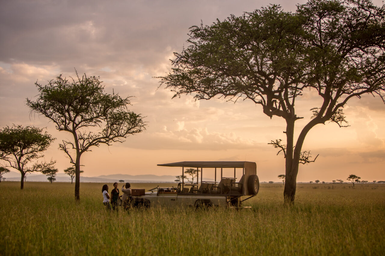 A couple on a game drive spot wildlife on the plains at Singita Grumeti, a honeymoon safari, Tanzania.