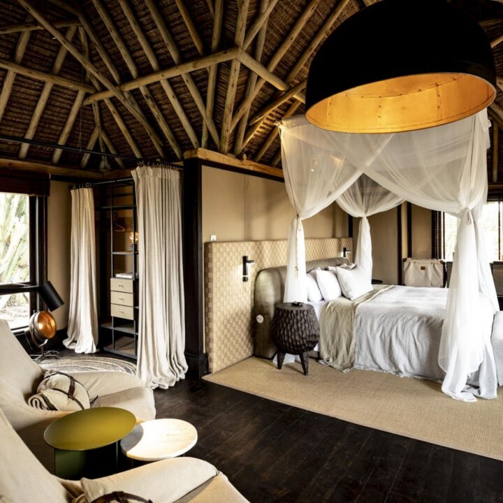 A gauzy canopy bed sits beneath soaring thatch and dark timber beams, luxury safari style, Segera Retreat, Kenya.