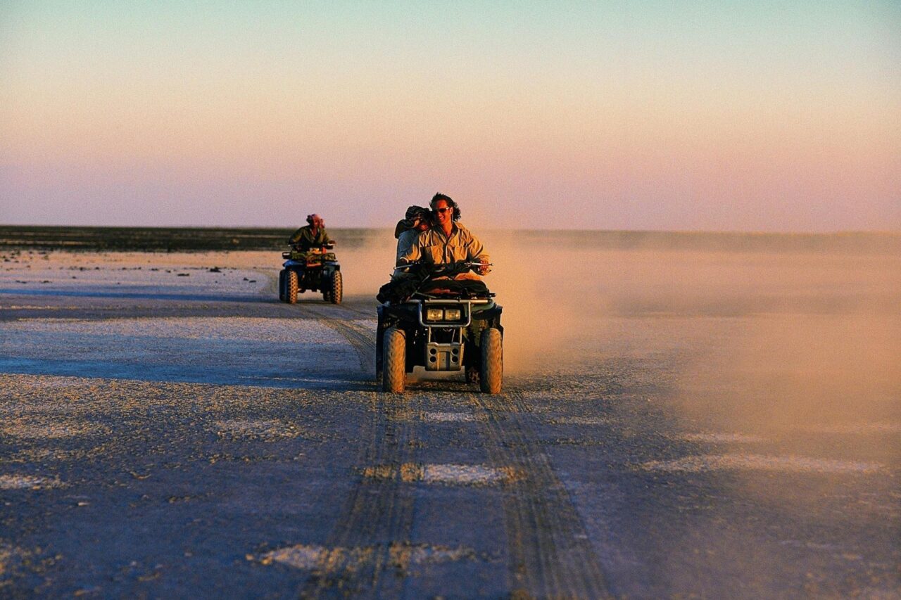 Riders on quad bikes cross the Makgadikgadi salt pans in warm early evening light, Botswana, on a luxury safari holiday.