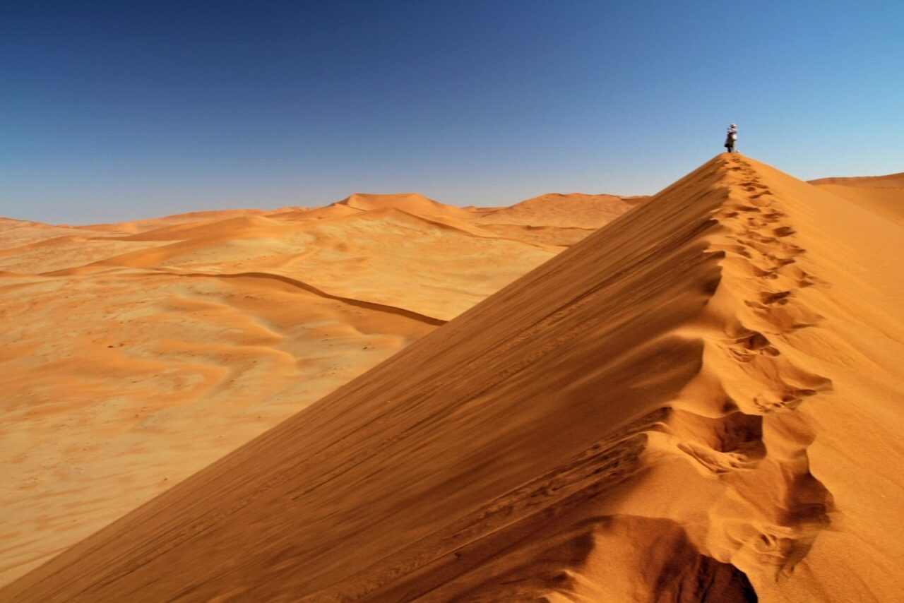 A lone figure stands on a vast orange dune in the Namib Desert, Namibia, part of a luxury safari holiday.