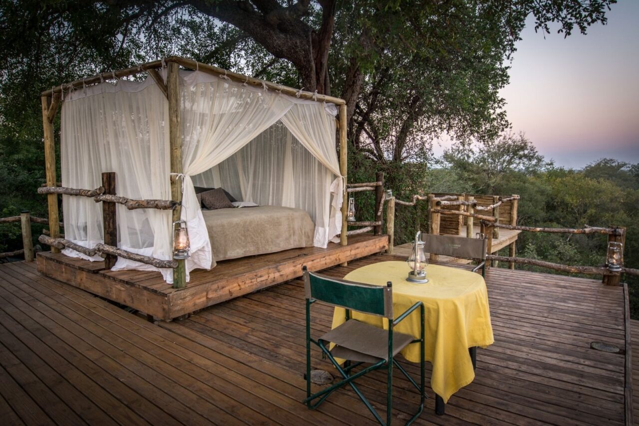 A table dressed in yellow linen sits beside the canopied sleep-out bed beneath the trees at Garonga, South Africa.