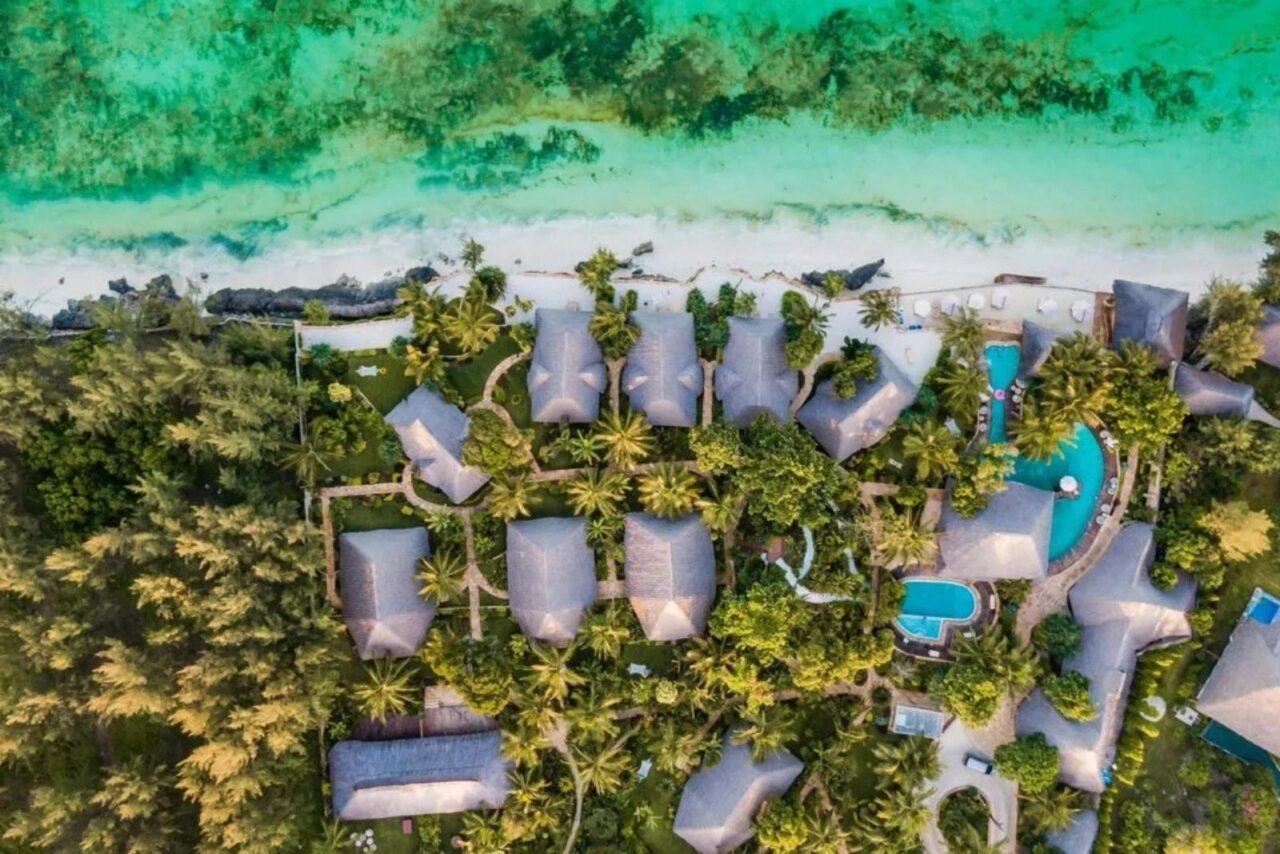 aerial view of lodge villas surrounded by trees in front of a beach in Zanzibar.